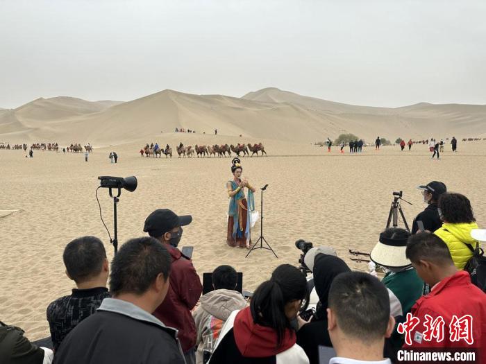 圖為2023年4月底，敦煌大漠“逐舞者”奧楠在鳴沙山月牙泉景區(qū)視頻直播，吸引游人圍觀。　馮志軍 攝